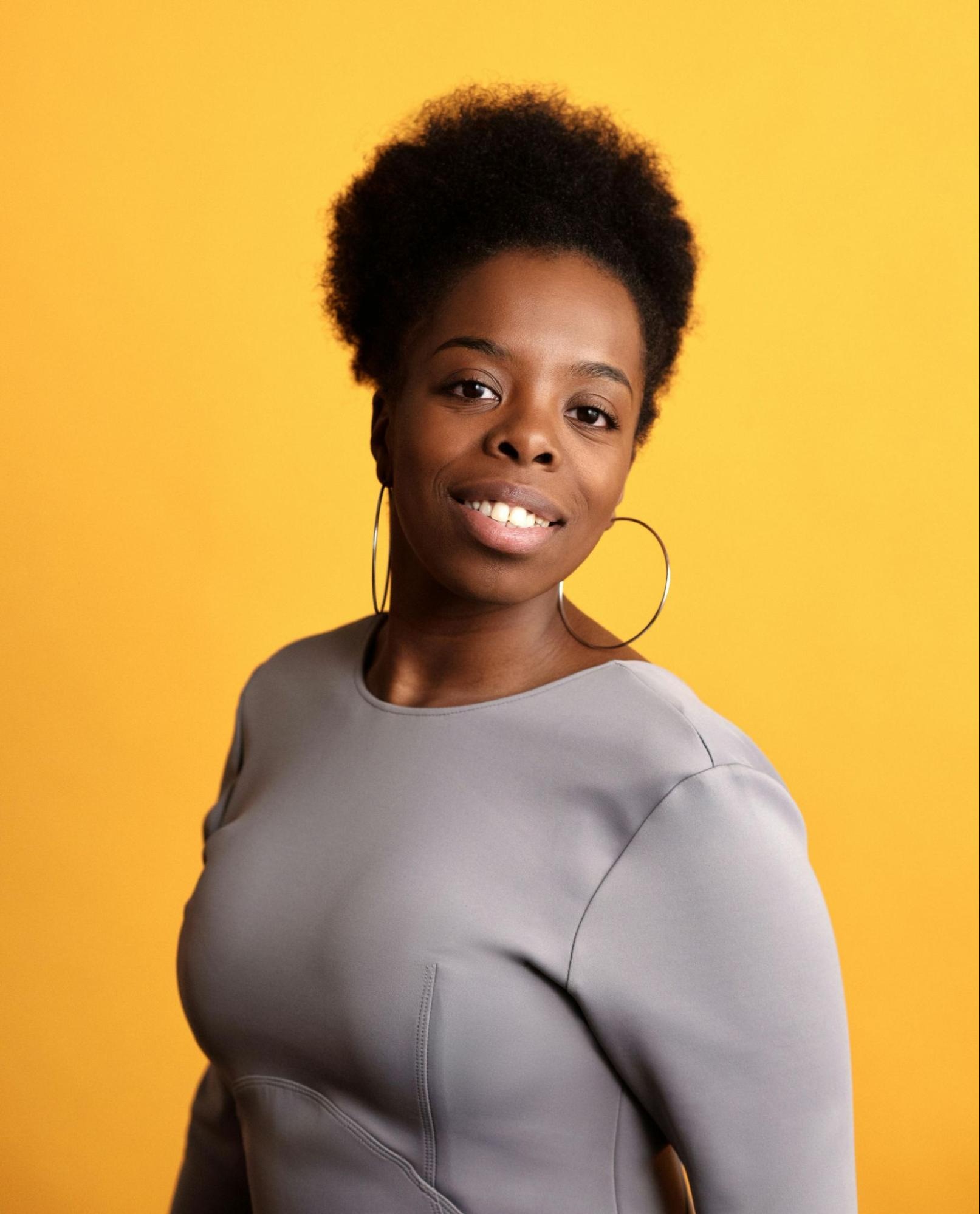 Professional headshot of woman with soft artificial lighting against a yellow background, creating a warm, flattering effect.
