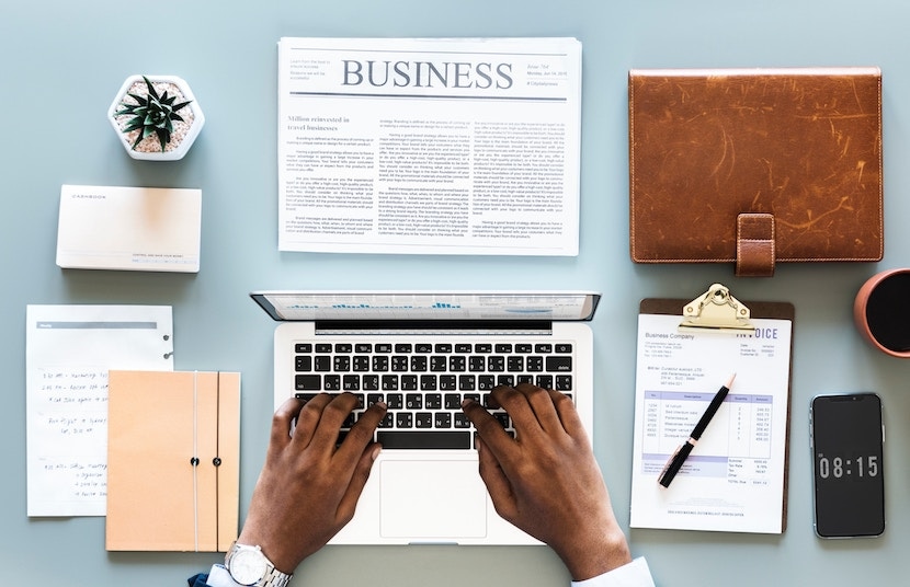 Top view of hands typing on a laptop in a business workspace with documents, a planner, and a smartphone.