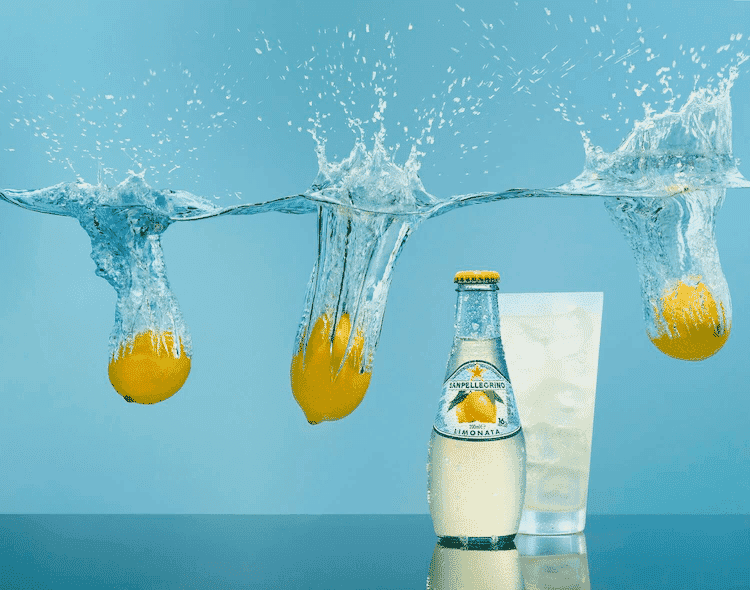 Sanpellegrino Limonata bottle with splashing lemons and glass in blue background