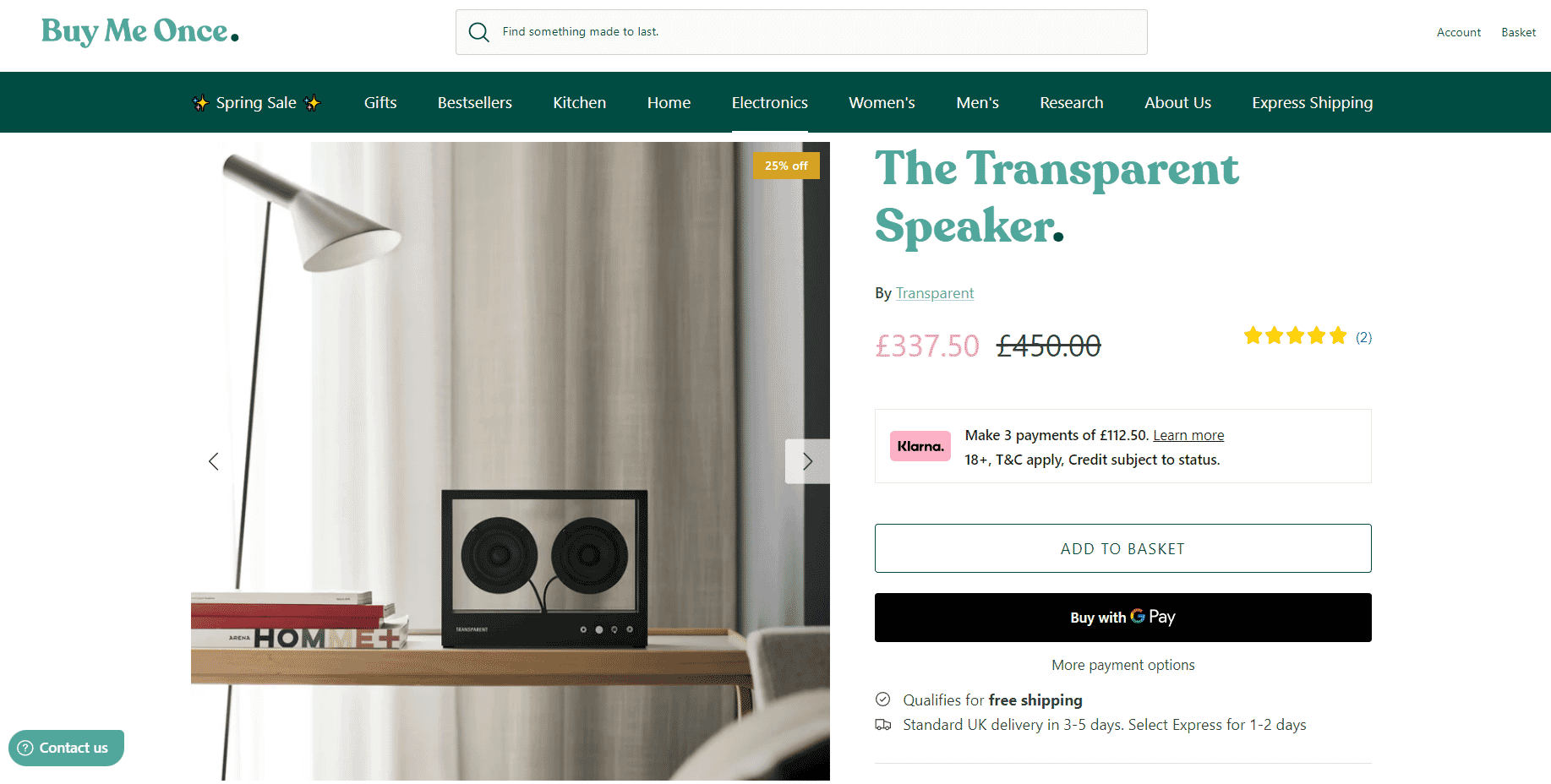 Transparent speaker displayed on a wooden shelf beside books and a minimalist lamp in a modern room setup.