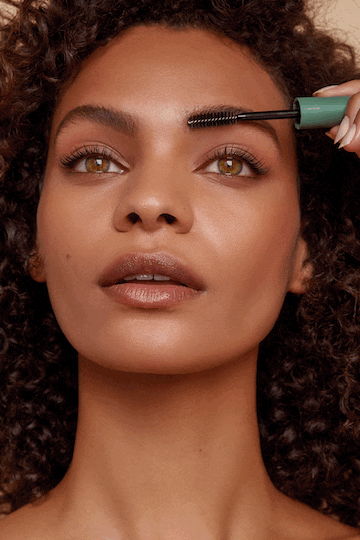 Close-up of woman with curly hair applying mascara to her eyebrows