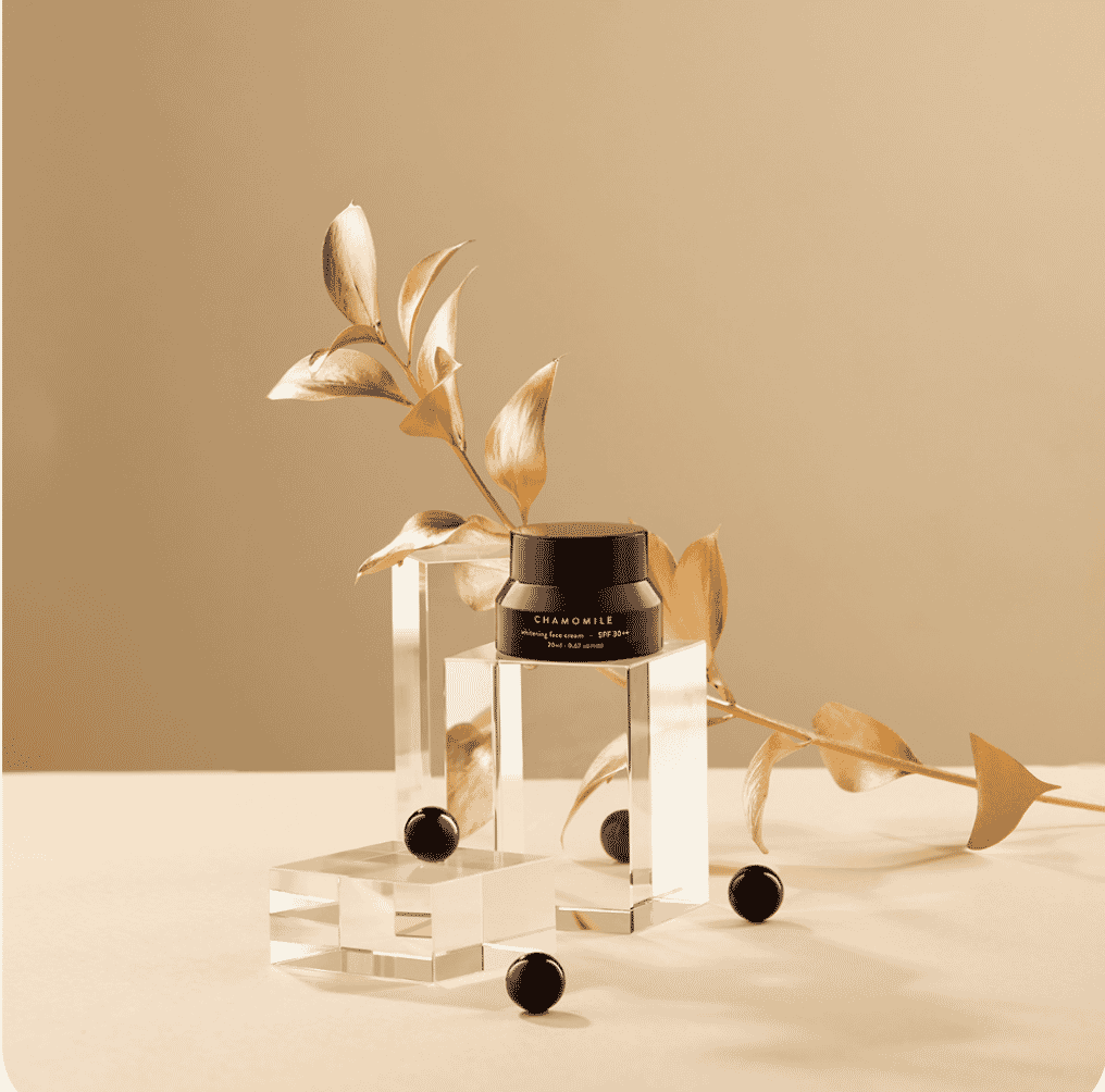Chamomile face cream jar on clear acrylic stands with gold botanical accent and black spheres