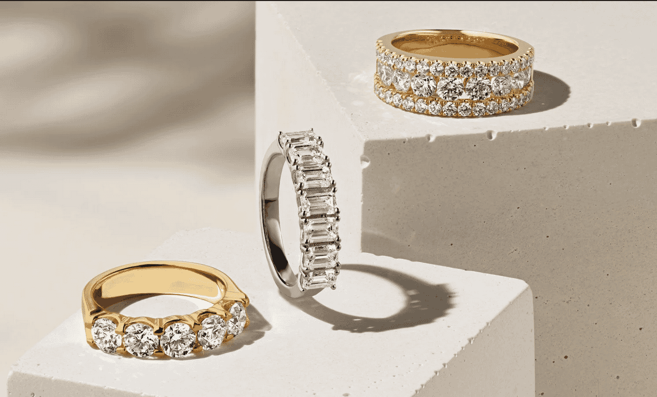 Three diamond rings in gold and silver displayed on white textured blocks with soft shadows