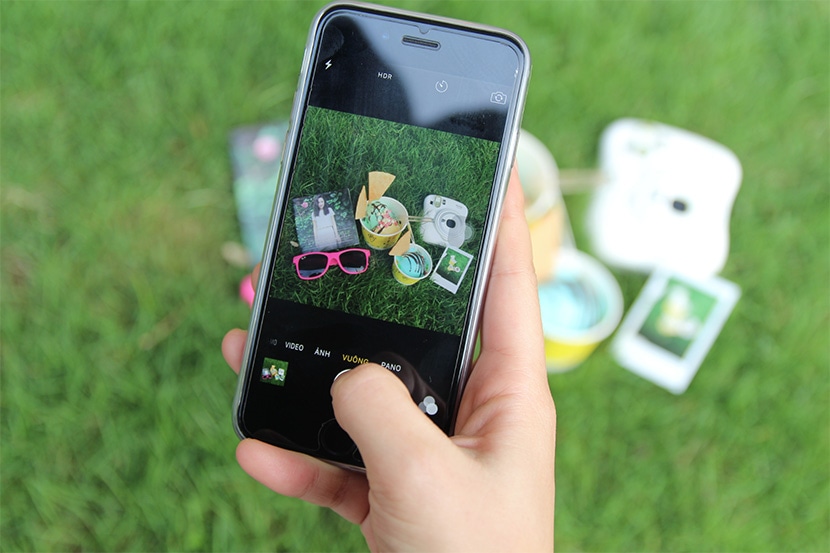 Hand holding smartphone photographing products on grass with colorful items in view