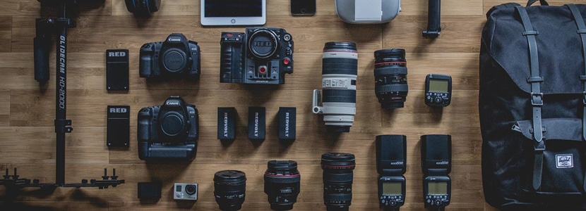 Assortment of professional photography equipment including cameras, lenses, and lighting gear arranged on a wooden surface
