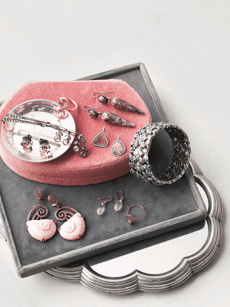 Assorted jewelry including earrings, rings, and bracelets arranged on a pink and gray velvet display tray.