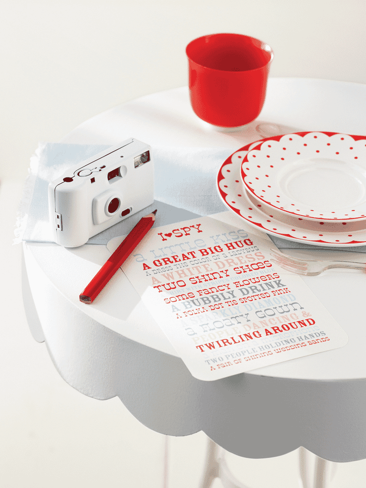 Table with a disposable camera, red cup, polka dot plates, and an I Spy game card.