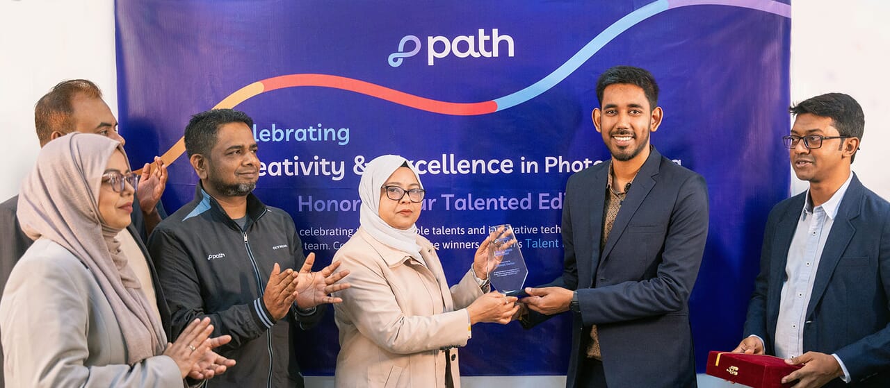 The COO of Path presents the first prize to the winner of the talent hunt program during an award ceremony. The event celebrates creativity and excellence in photo editing, with team members applauding in front of a branded backdrop.
