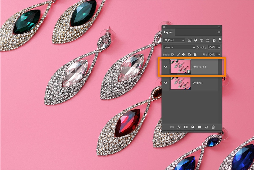 Photoshop layers panel showing added lens flare effect layer on jewelry earrings against a pink background to enhance sparkle.