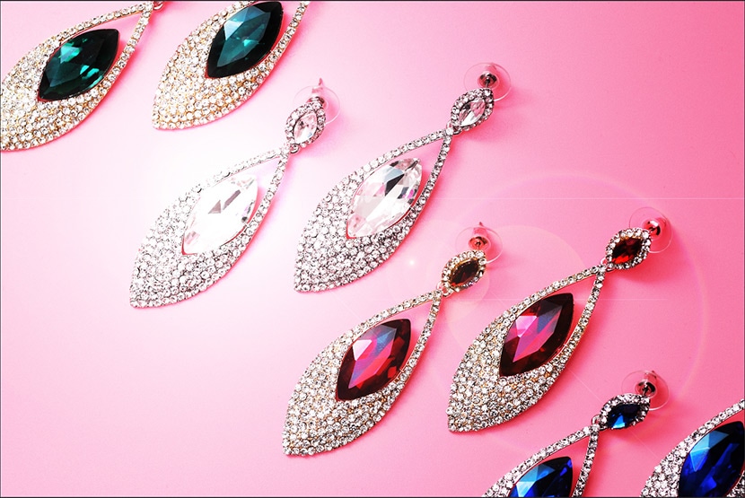 Jewelry earrings with gemstones on a pink background, showcasing final enhanced sparkle and lens flare effect for added brilliance.