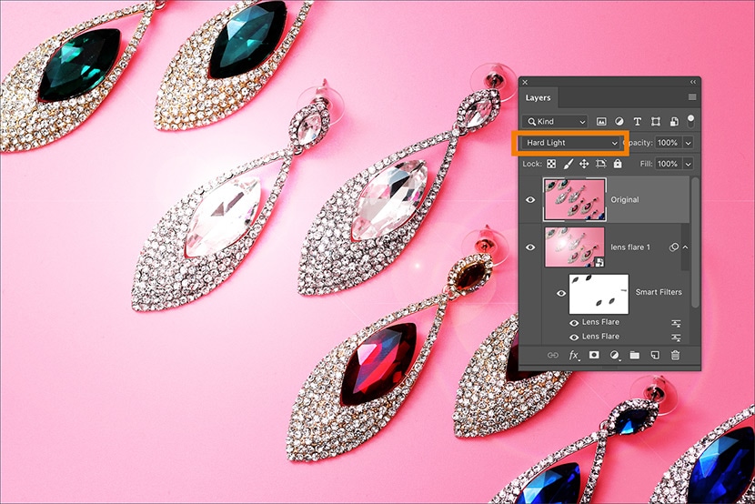 Photoshop interface with Hard Light blend mode applied to masked lens flare layer on jewelry earrings with gemstones on a pink background.