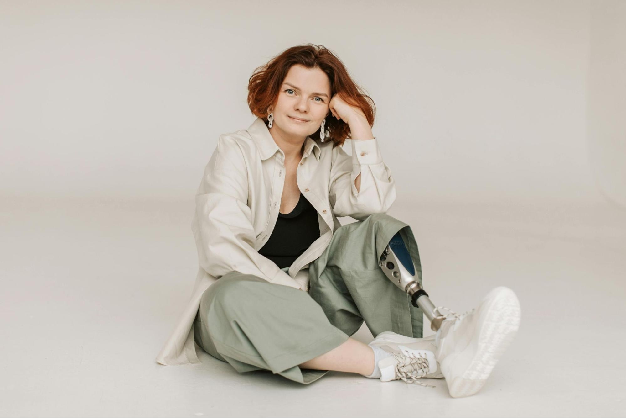 portrait on off-white background of  a woman sitting down casually, she has a prosthetic leg
