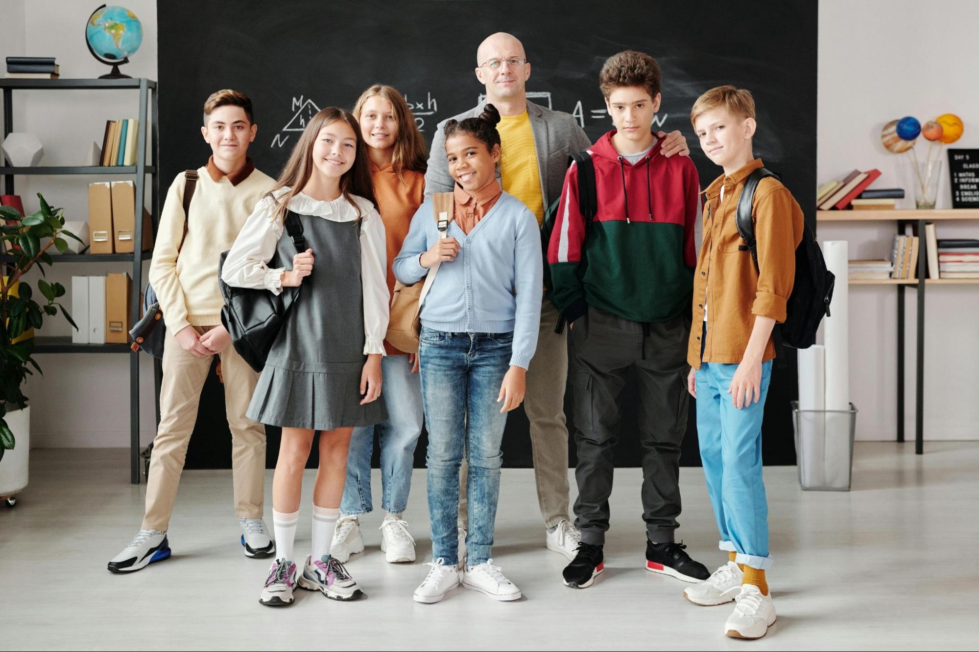 portrait photo of a group of students and their teacher in front of a blackboard