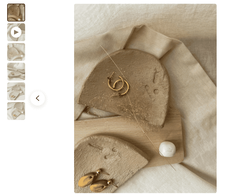 Gold earrings displayed on a textured natural background with neutral tones and artistic composition