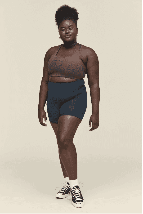 Woman modeling athletic wear: dark sports bra, high-waisted shorts, and sneakers.