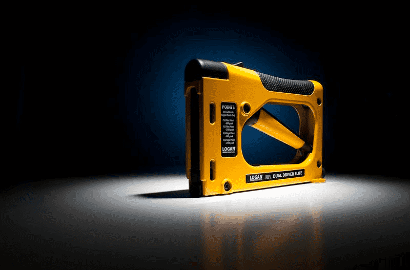 Yellow Logan Dual Driver Elite staple gun with black grip on dark, spotlighted background.