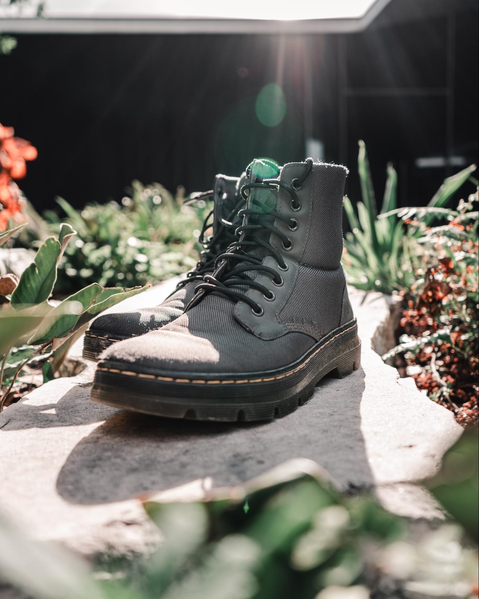 Black lace-up boots on a stone surface with natural sunlight and green foliage in the background