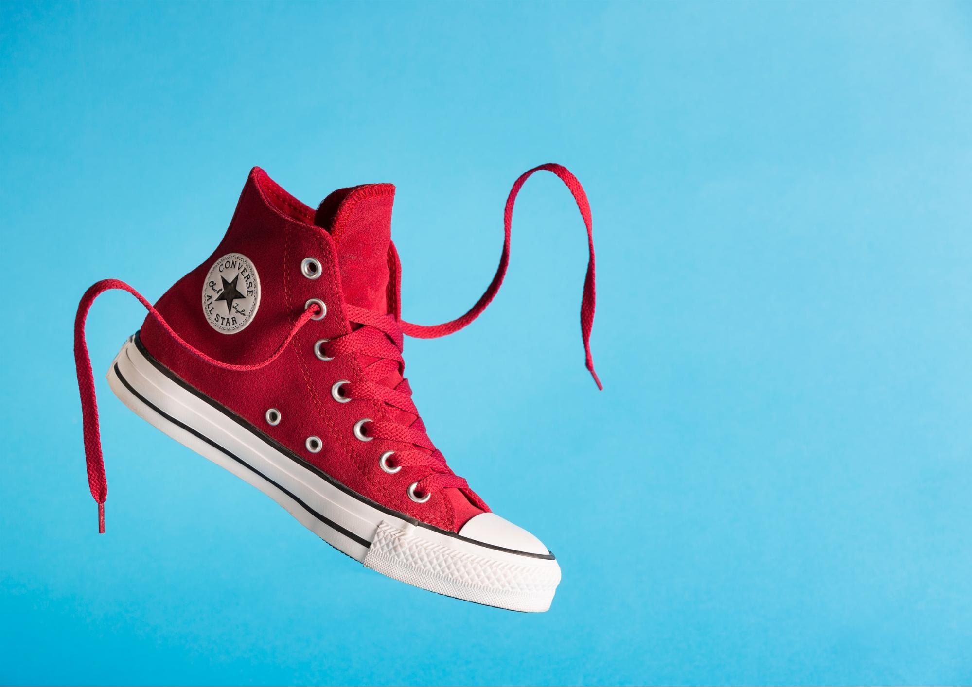 Red Converse high-top sneaker with laces floating against a vibrant blue background