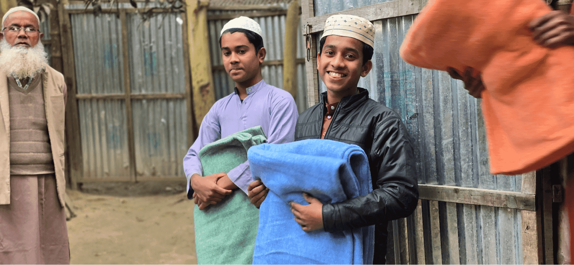 boy smiling and looking at camera holding a blanket with another boy in the background looking at the ground and holding a blanket