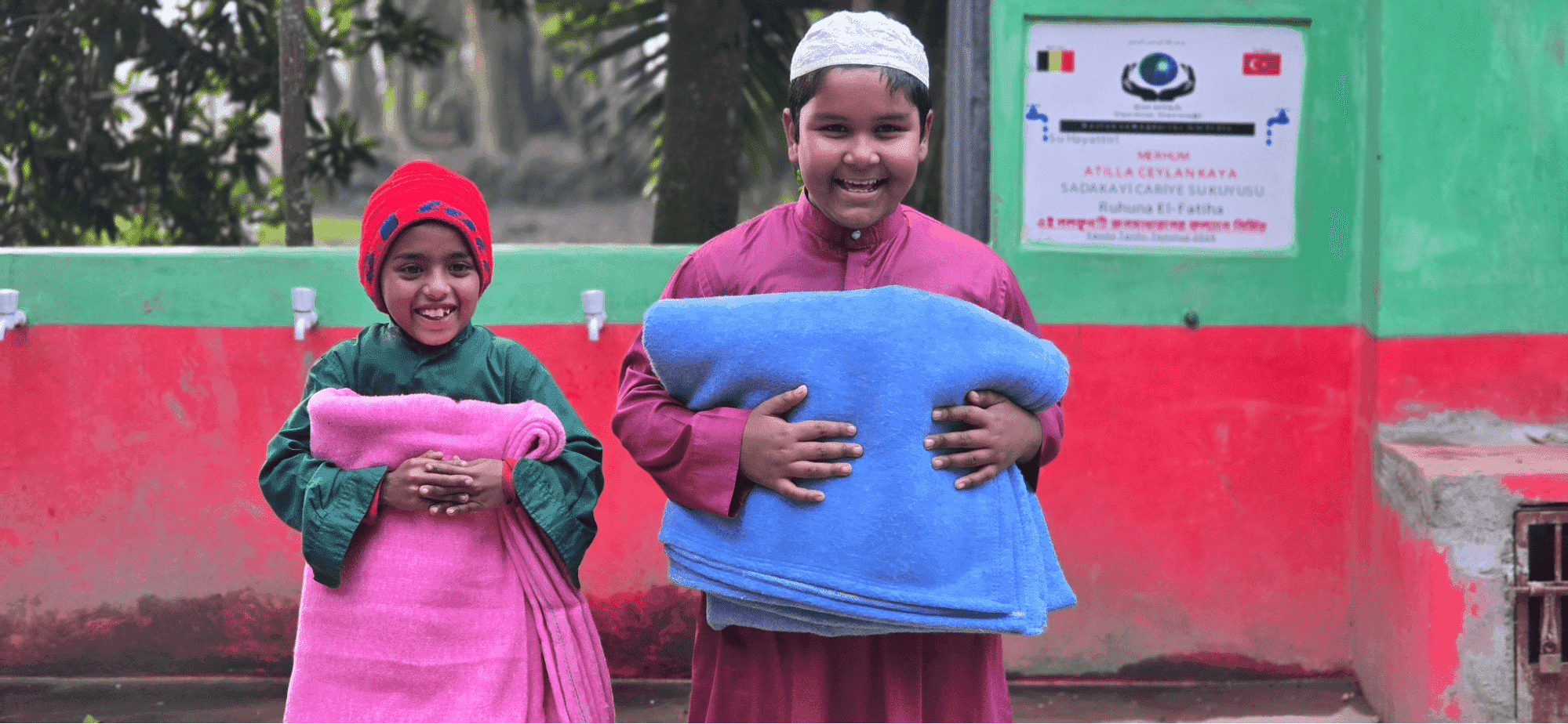 two boys smiling and holding blankets while looking at the camera
