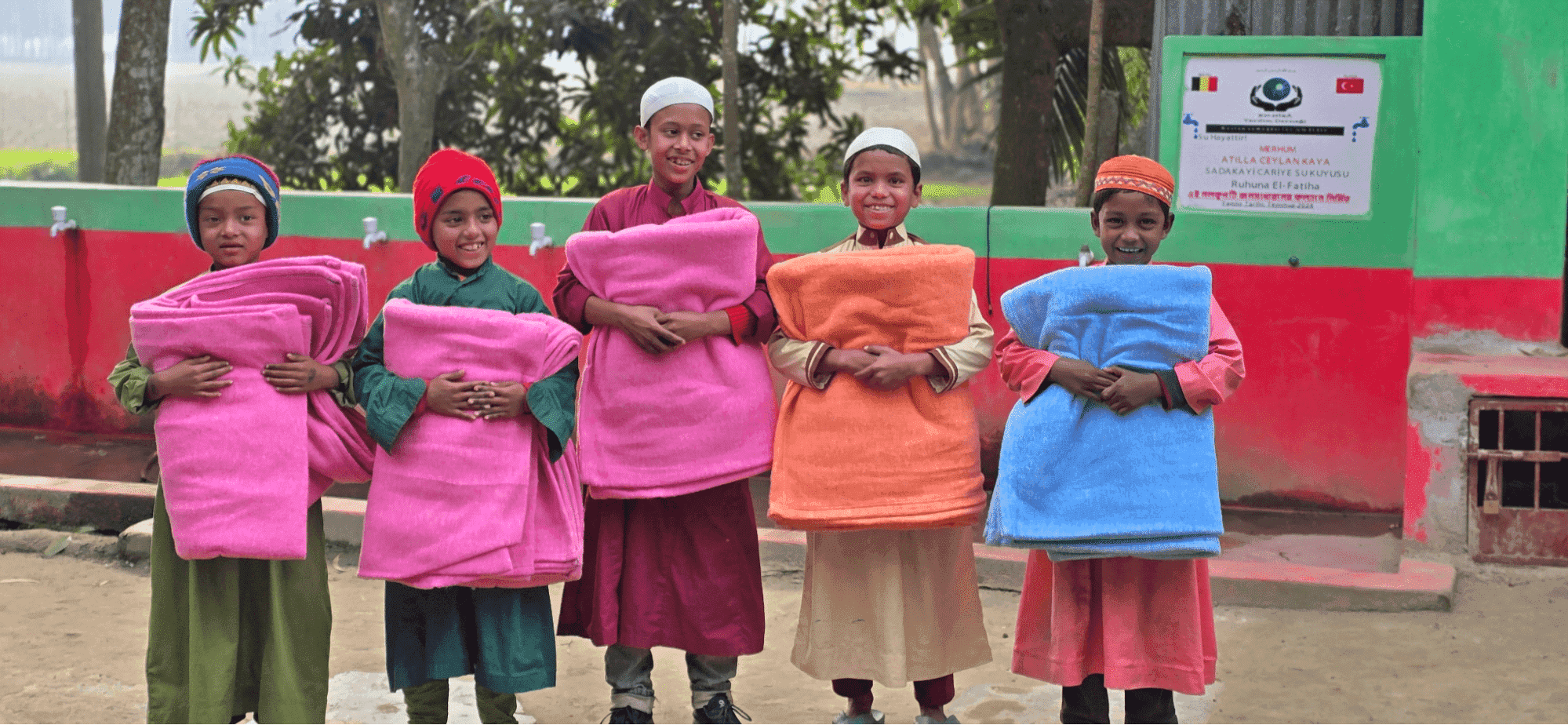 five boys smiling and holding colorful folded blankets in front of them