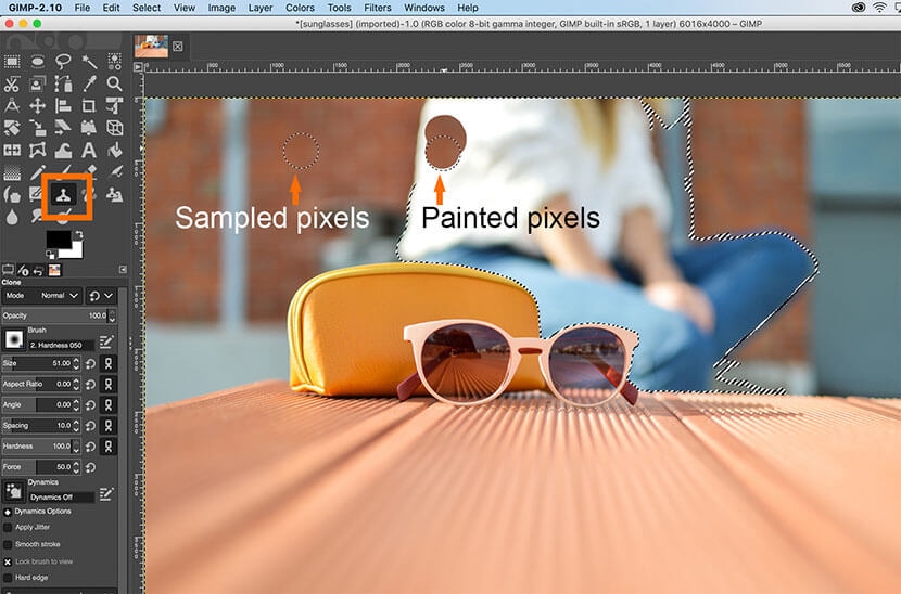 GIMP workspace with Clone Tool used for object removal, showing sampled and painted pixels on image.