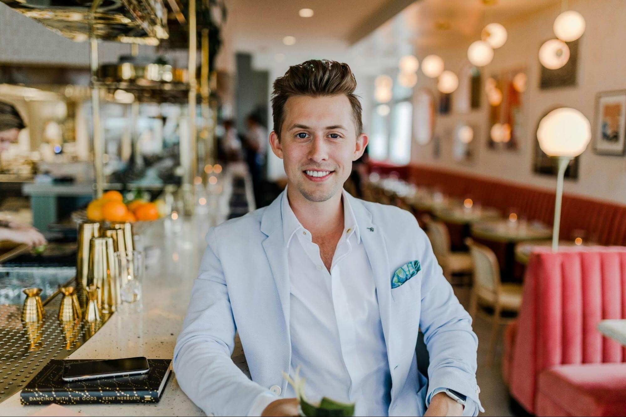Half-body headshot of a man in a casual setting, seated at a bar with a blurred background for context