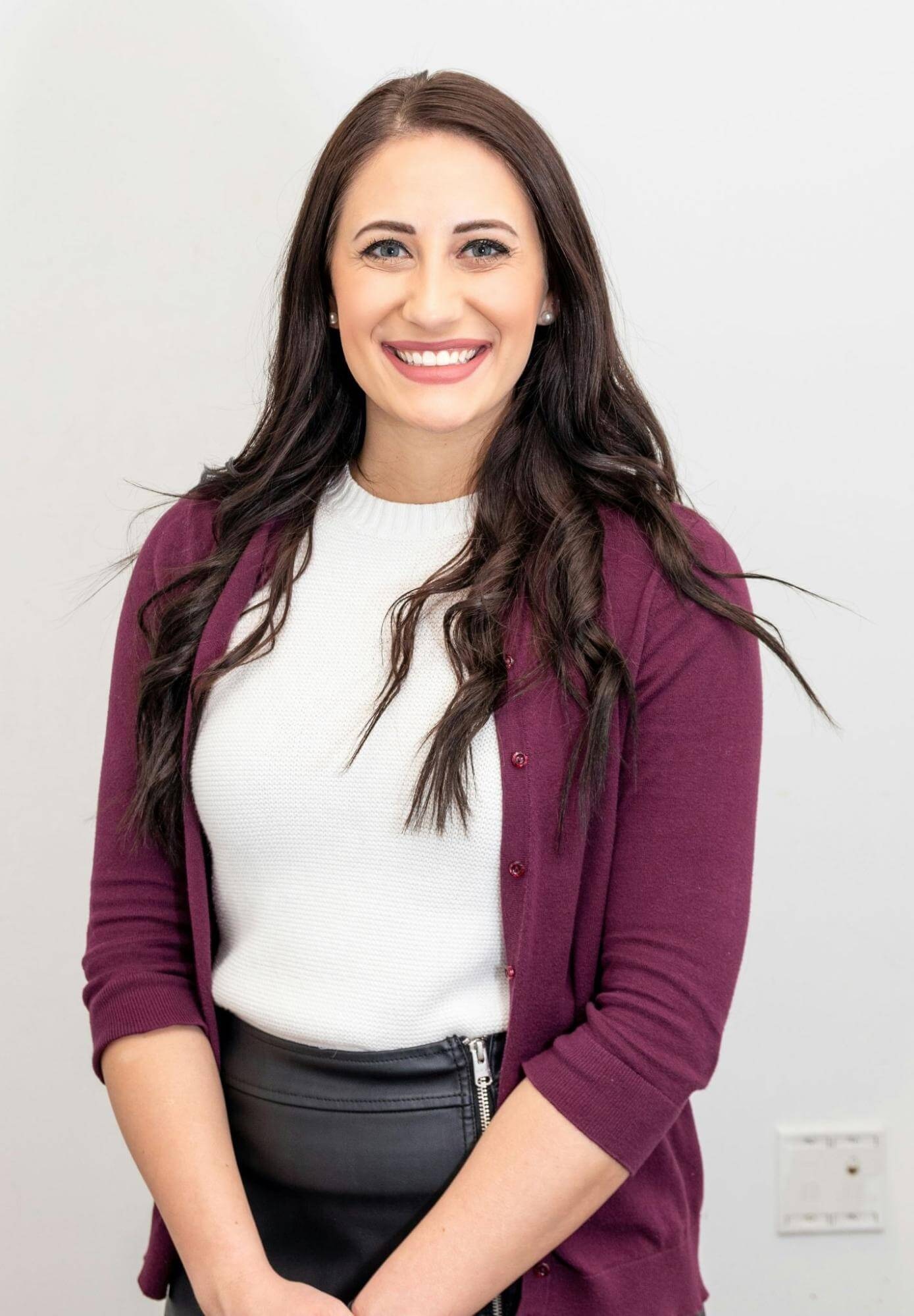 Smiling woman in professional attire against a plain background, half-body headshot