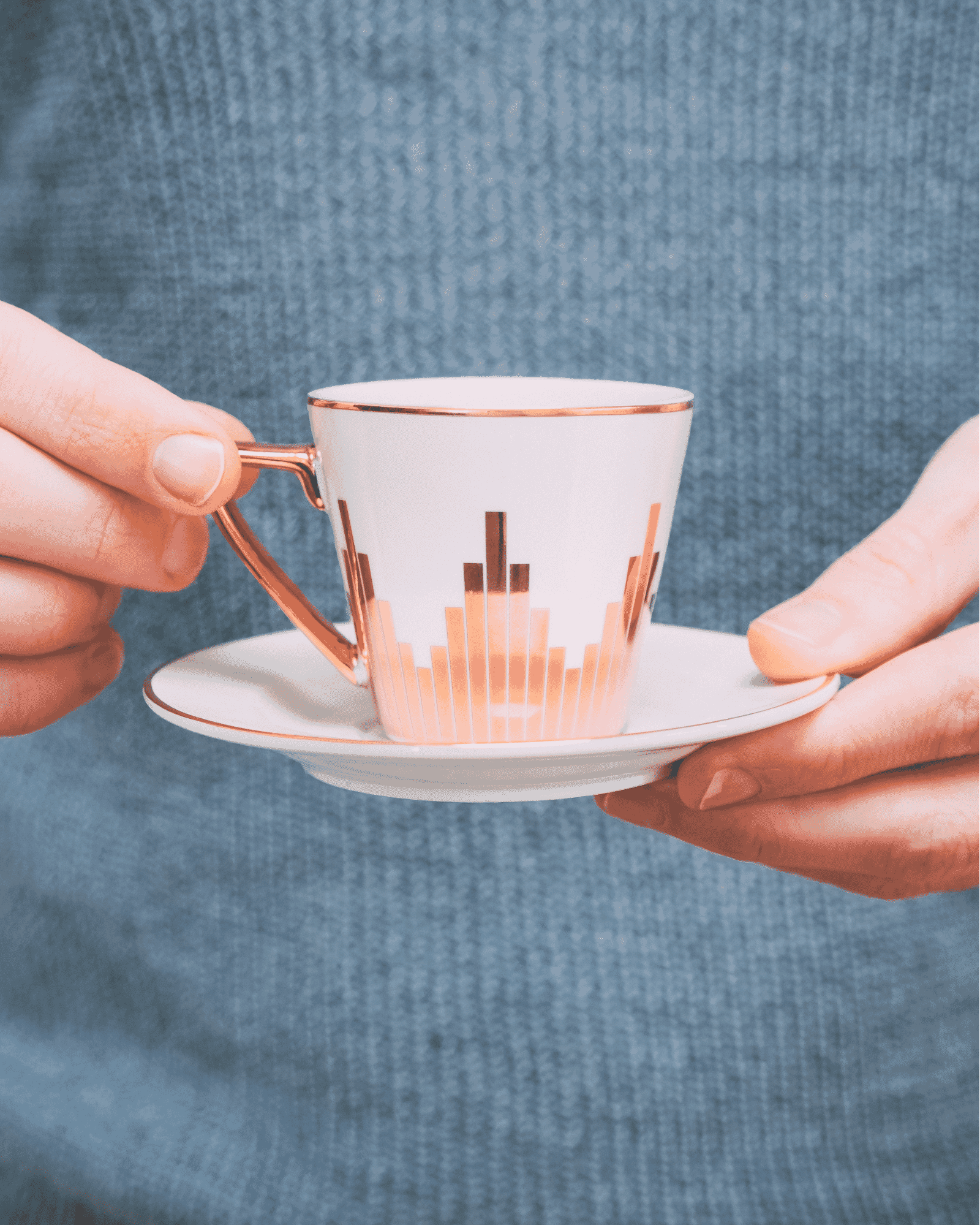 Hands holding a white teacup with Art Deco gold accents on a matching saucer, highlighting product detail.