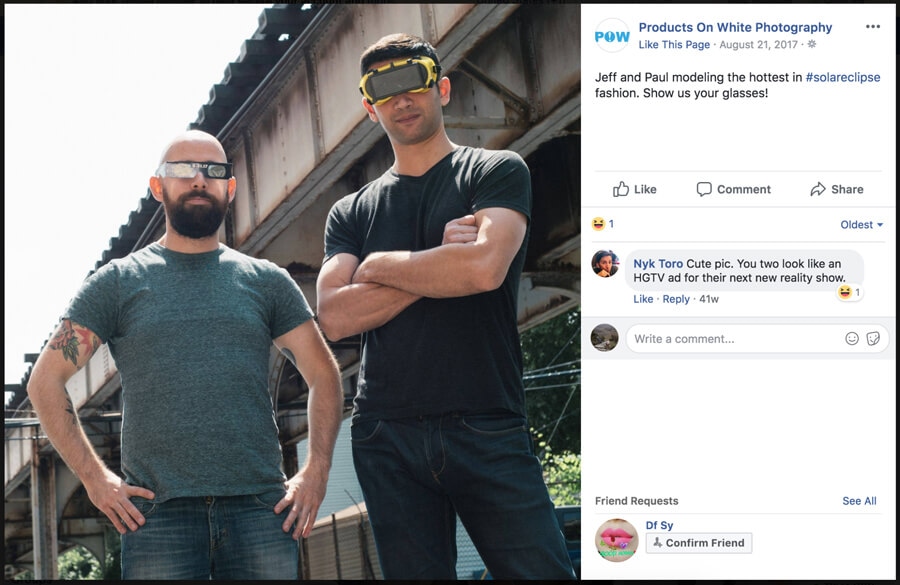 Two men posing outdoors wearing protective solar eclipse glasses under a metal bridge structure.