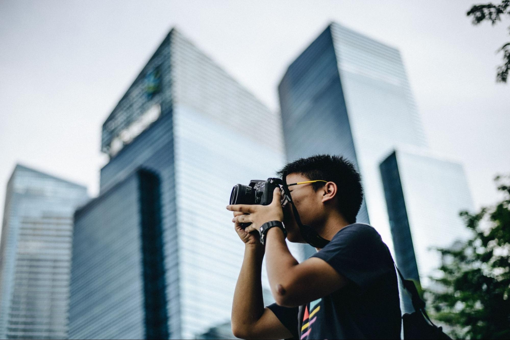 Photographer capturing cityscape against tall modern buildings in an urban setting.