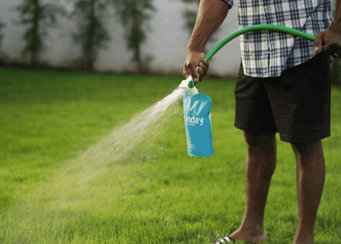 Person applying lawn treatment with a hose attachment, spraying evenly across a green lawn.